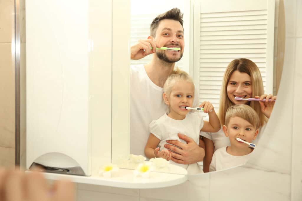 All family brushing their teeth together, looking in the mirror