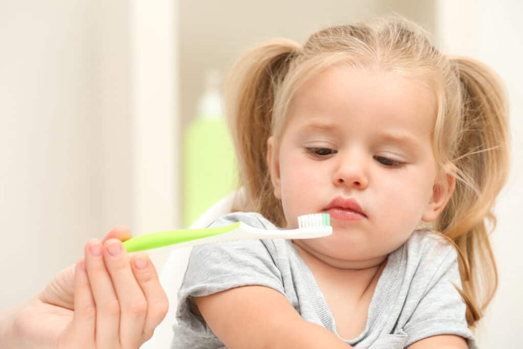 The little girl looks suspiciously at the toothbrush