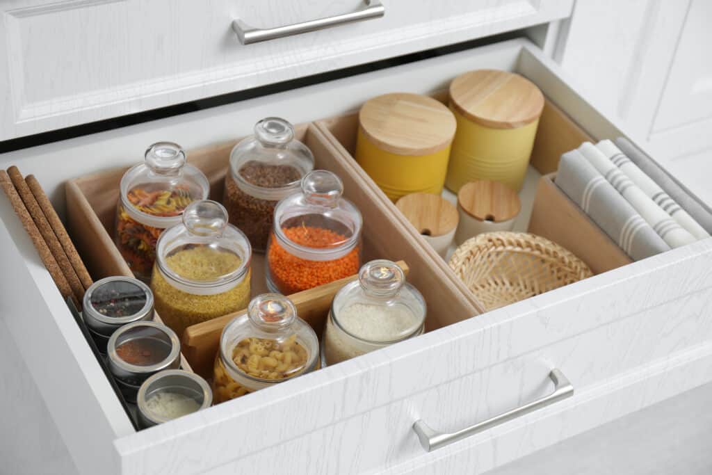 Open drawer with different jars indoors, closeup. Order in kitchen