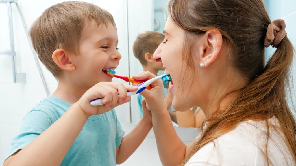 Smiling little boy with young mother brushing teeth and cleaning mouth with toothbrushes to each other. Family having fun while taking care of teeth hygiene and healthcare.